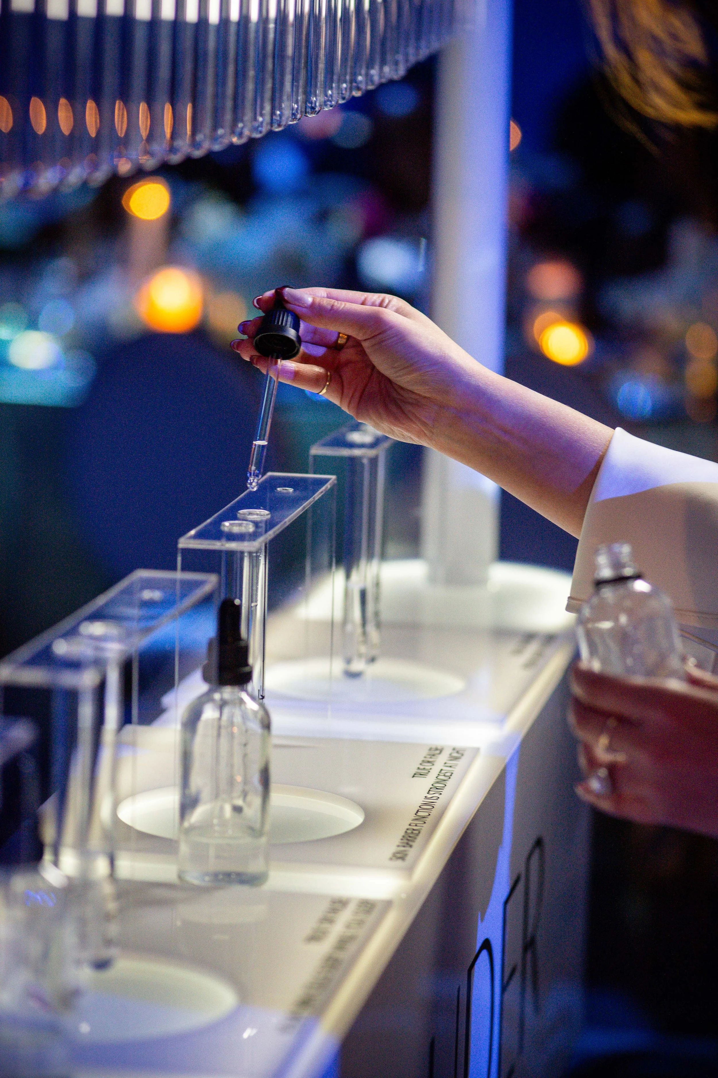 A person using a dropper to place liquid samples into test tubes at an outdoor event during night time, with city lights in the background.