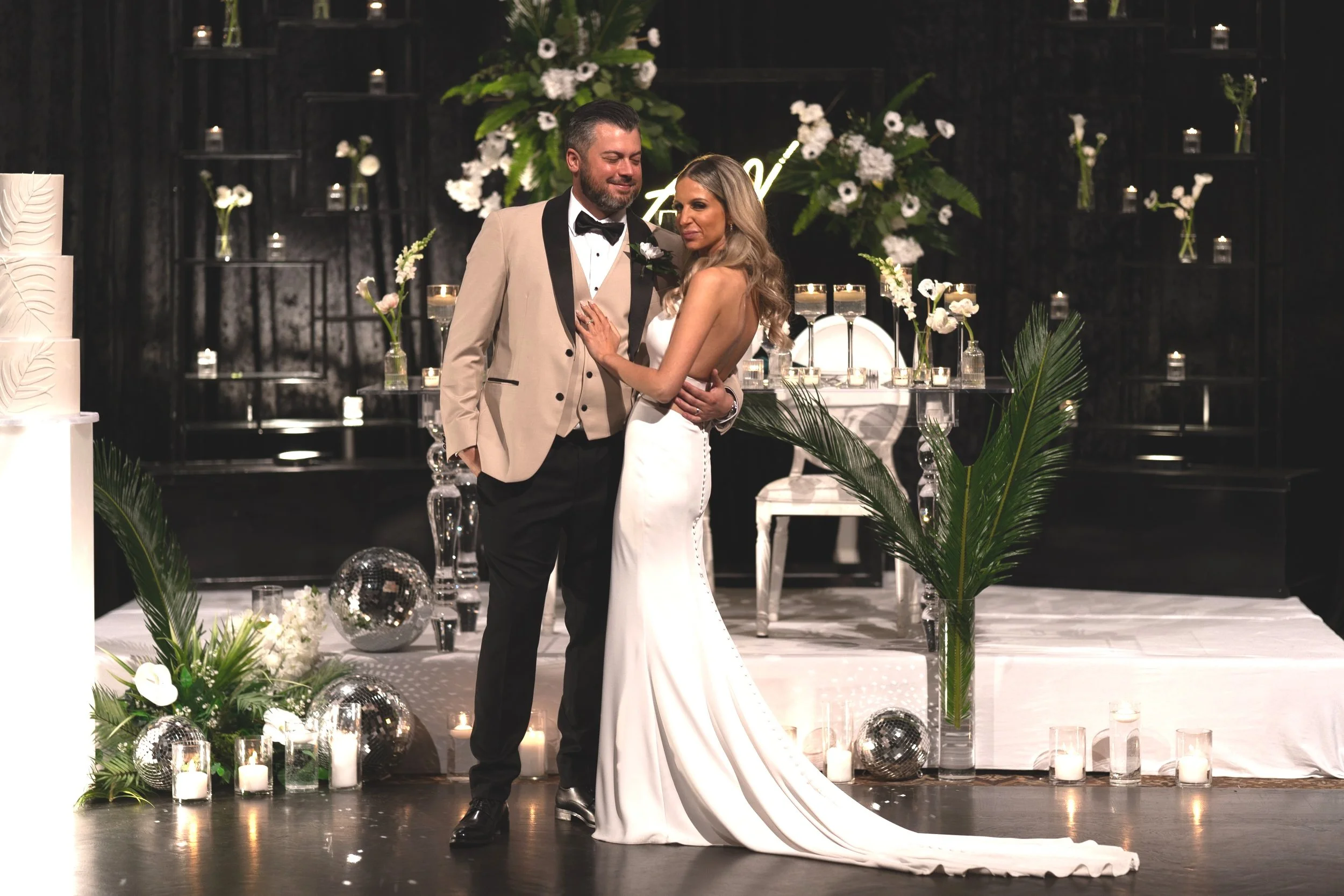 A bride and groom dancing at their wedding reception, surrounded by candles, flowers, and decorative items in a dimly lit room.