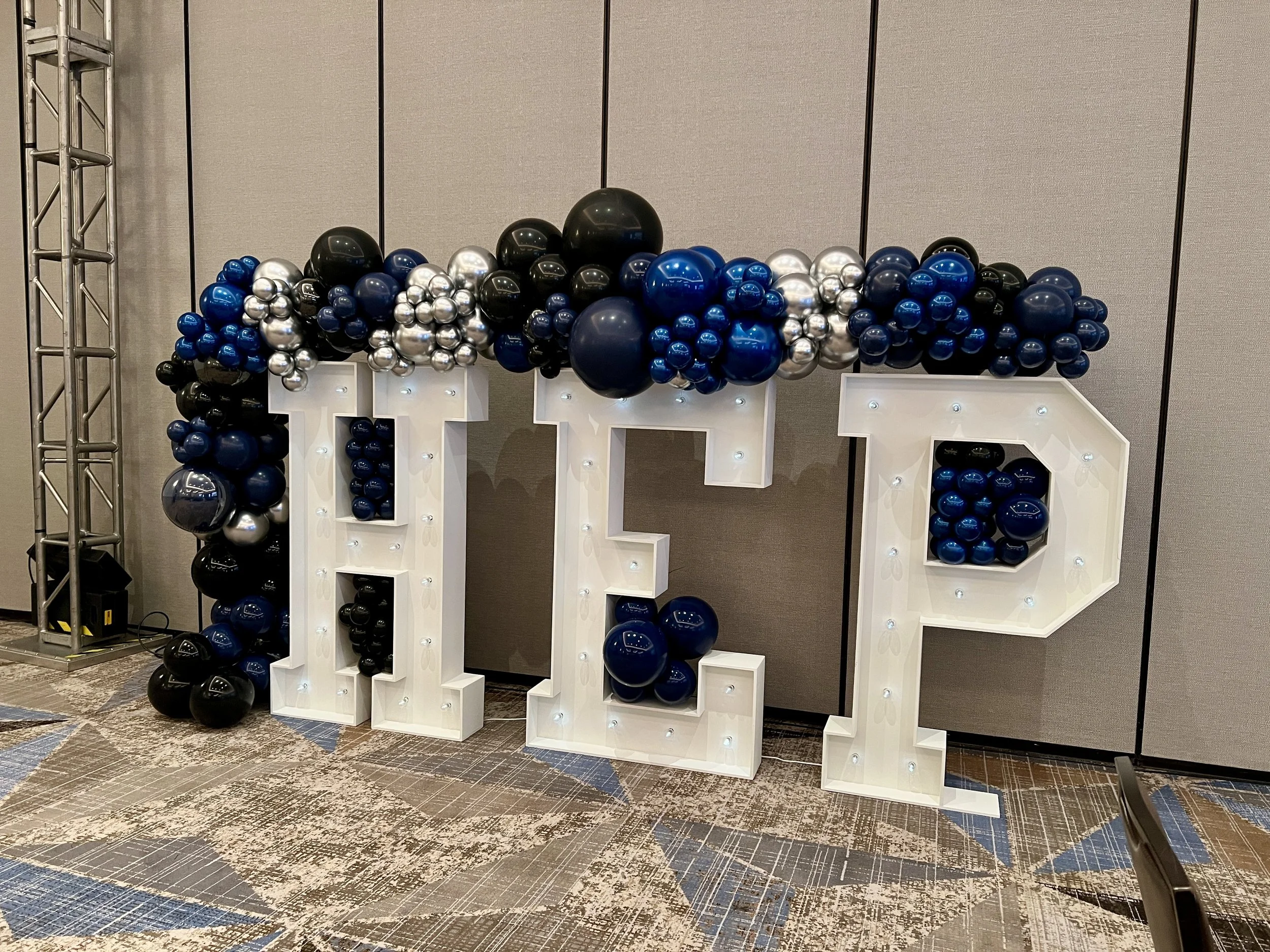 Illuminated corporate marquee letters with a modern organic balloon garland in navy blue, royal blue, black, silver, and chrome for a corporate event in San Antonio, Texas.