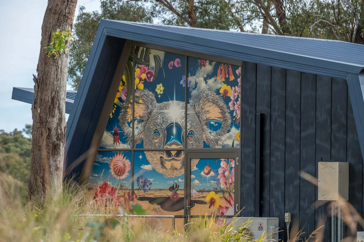 A building with a colorful mural of a koala's face surrounded by flowers and clouds on the front window.