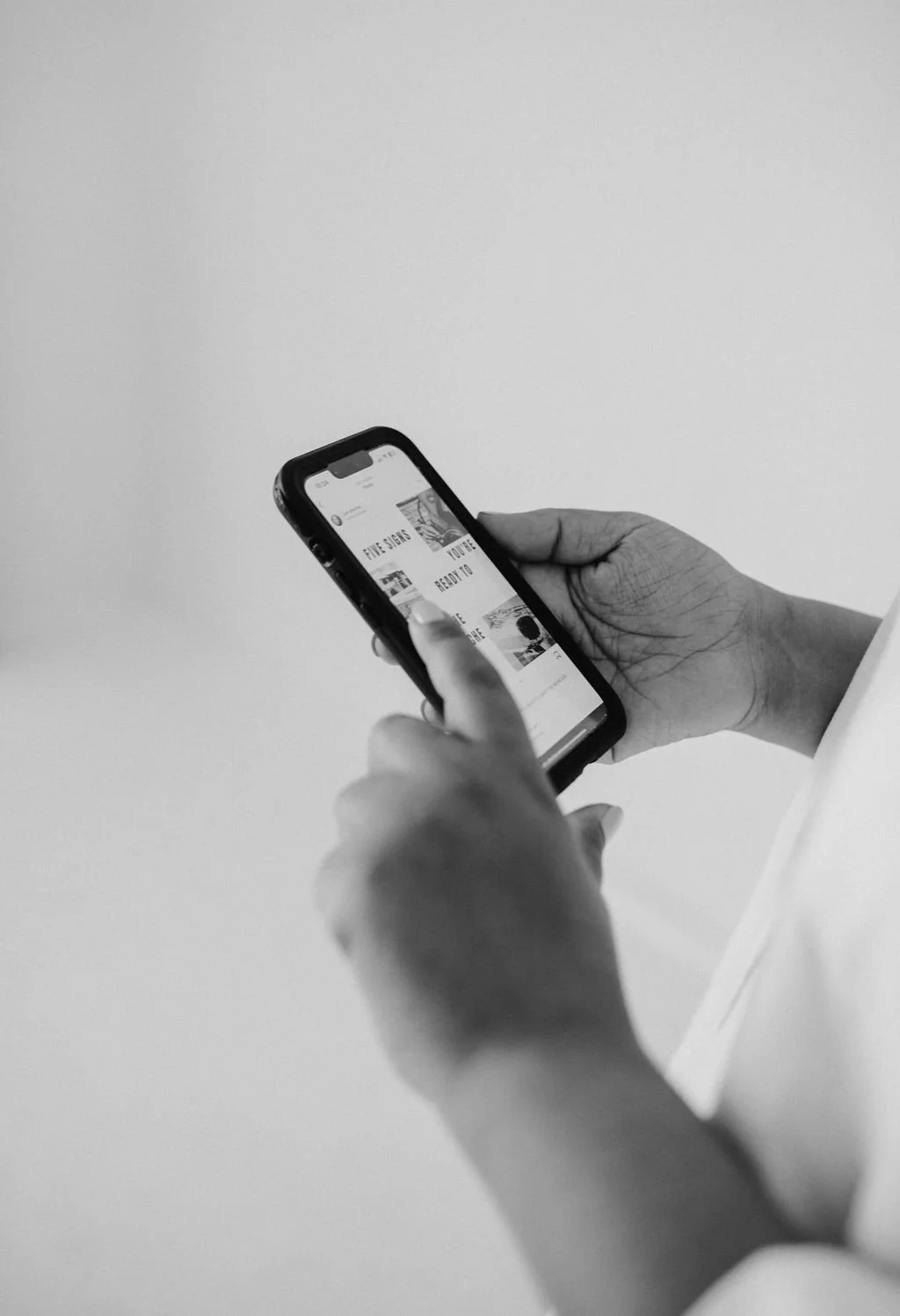 Black and white photo of two hands holding an iPhone displaying an Instagram carousel post titled "Five signs you're ready to..."