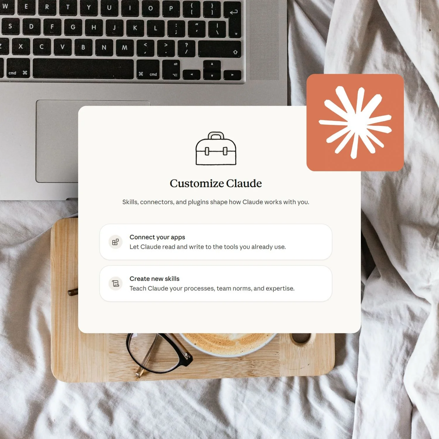 Mockup of a "Customize Claude" panel showing app-connection and skill-creation options, over a photo of a laptop keyboard, coffee cup and glasses on a wooden tray.