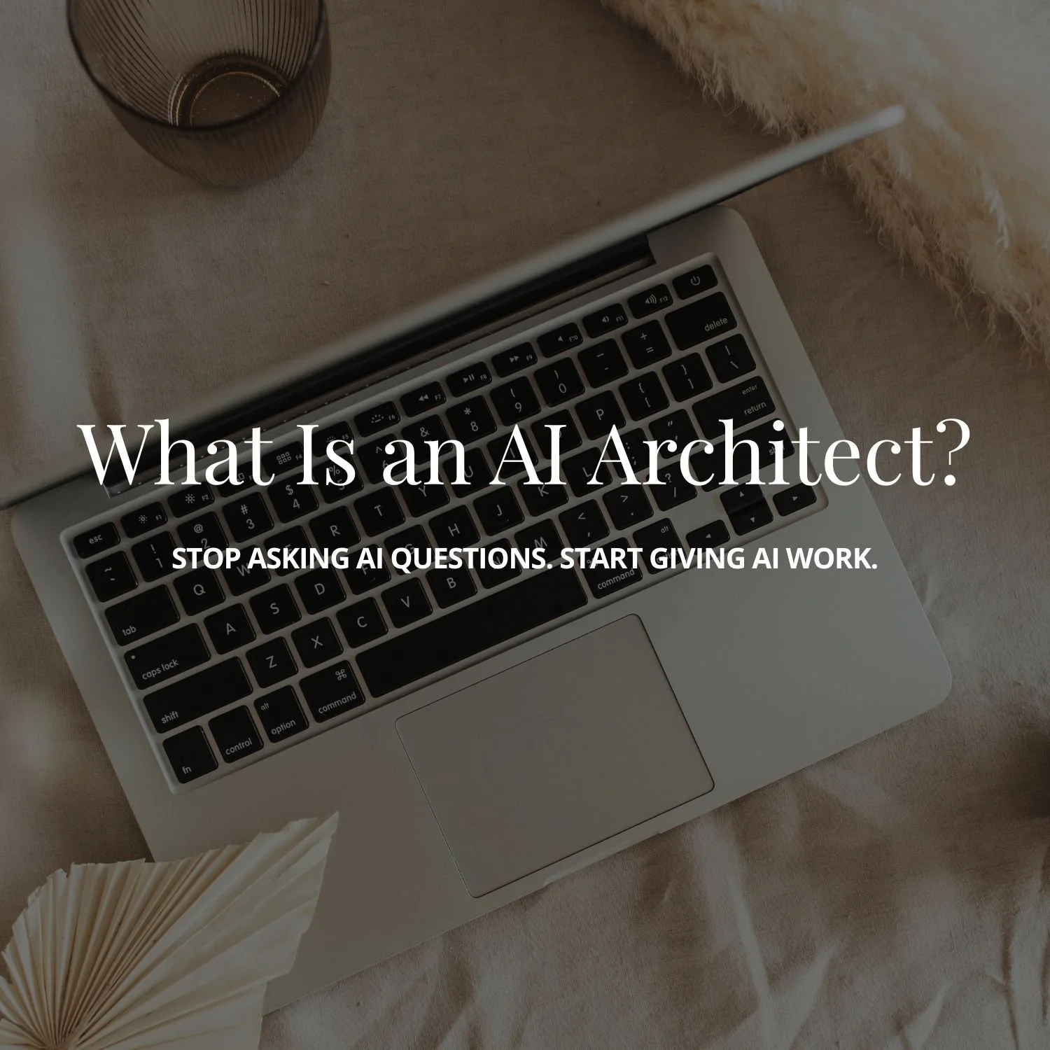 Overhead photo of a laptop keyboard on a bed with a glass and a decorative paper fan nearby, overlaid with the title "What Is an AI Architect?" and subtitle "Stop asking AI questions. Start giving AI work."
