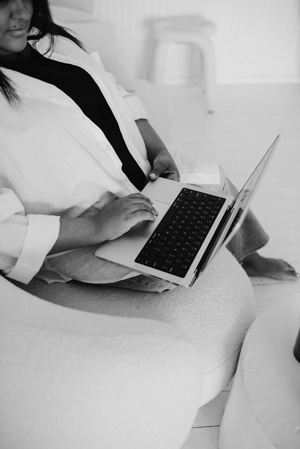 Black and white close-up of Sherise Adkins' hands typing on a laptop keyboard while seated in a white bean bag chair
