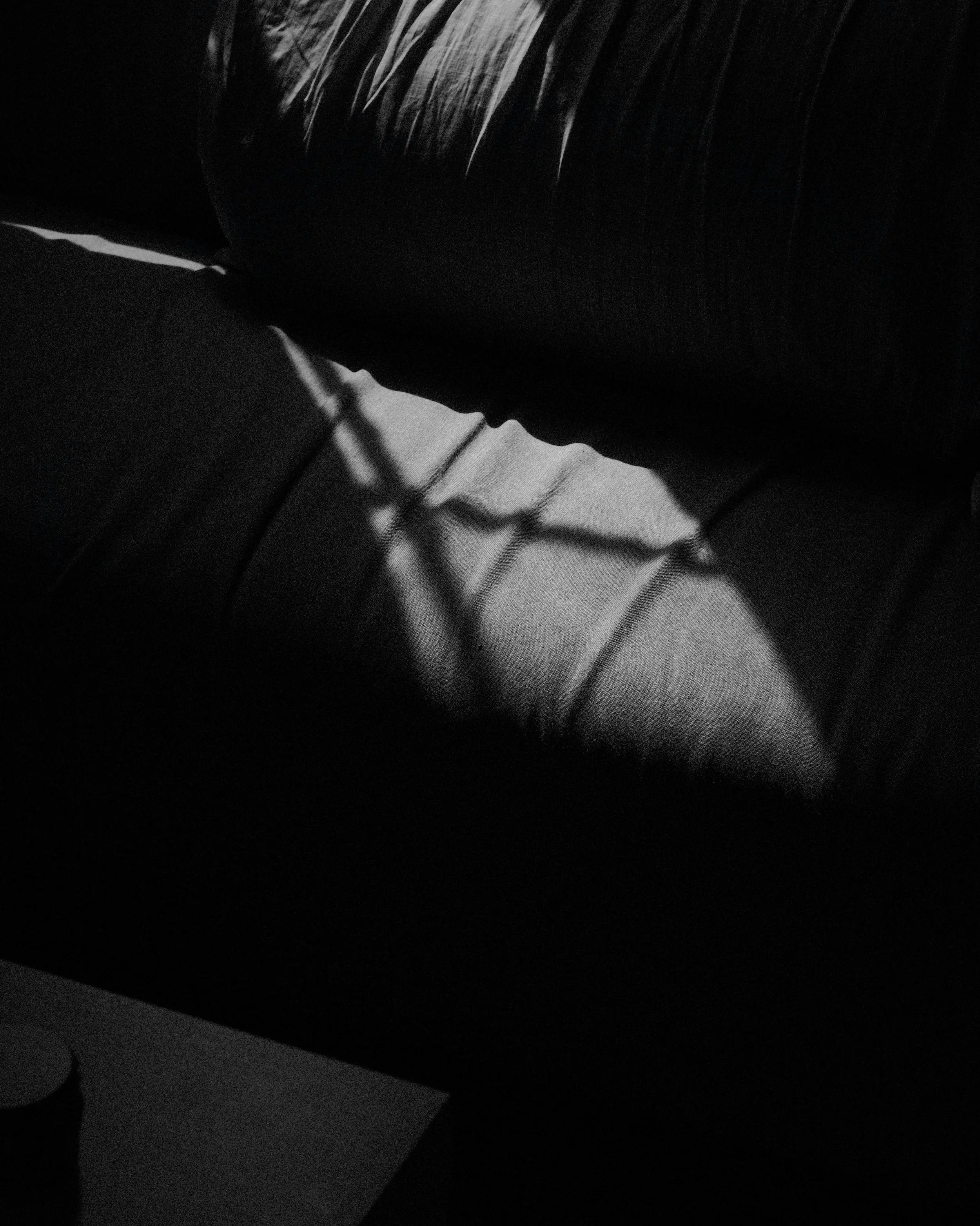 Black and white close-up of window-blind shadows falling across a sofa cushion