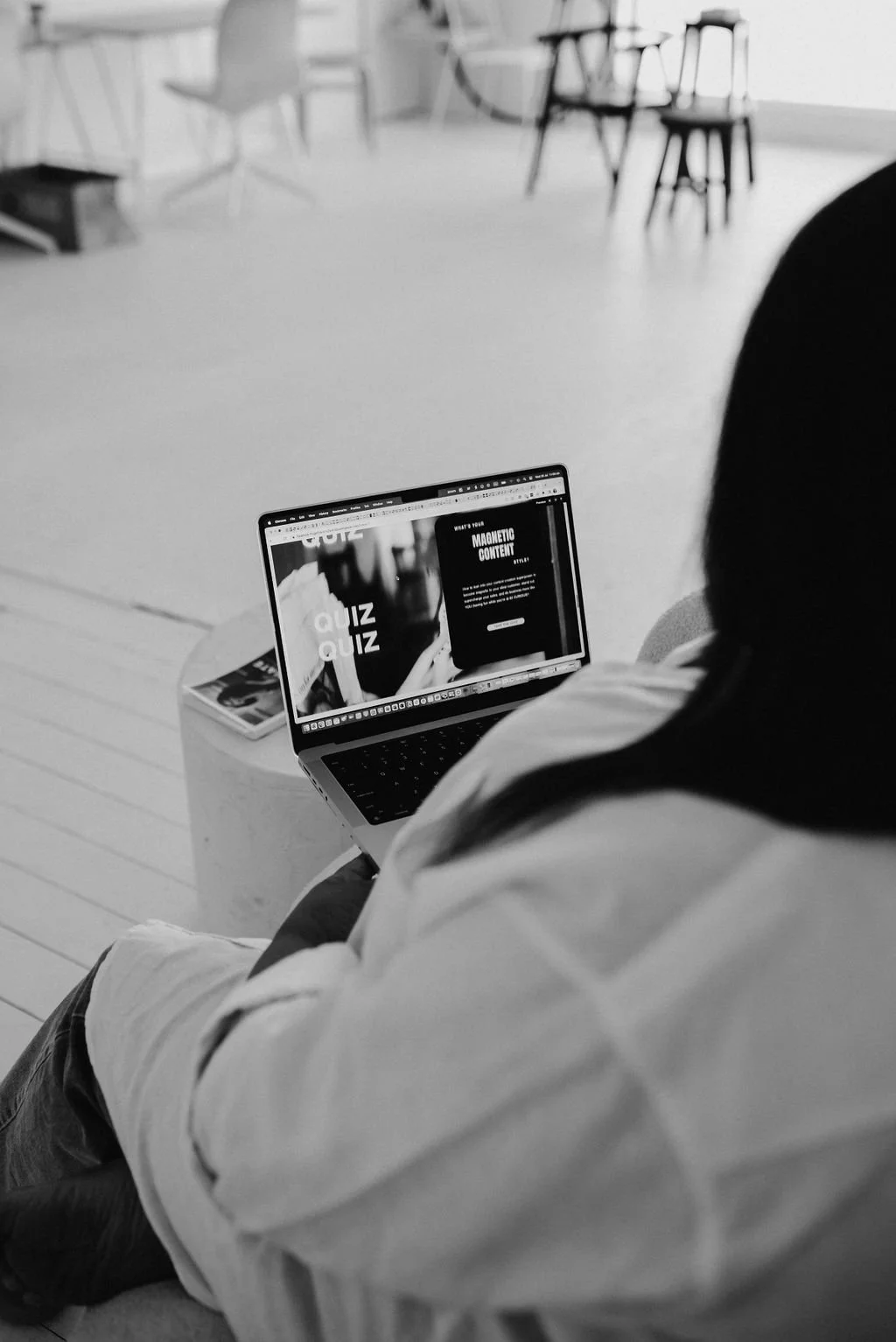 Black and white photo of someone sitting with a laptop open to a website design featuring a quiz page