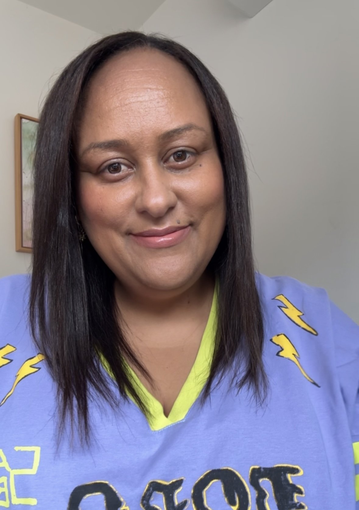 Sherise Adkins smiling in a selfie-style photo, wearing a purple graphic jersey with yellow lightning bolt details