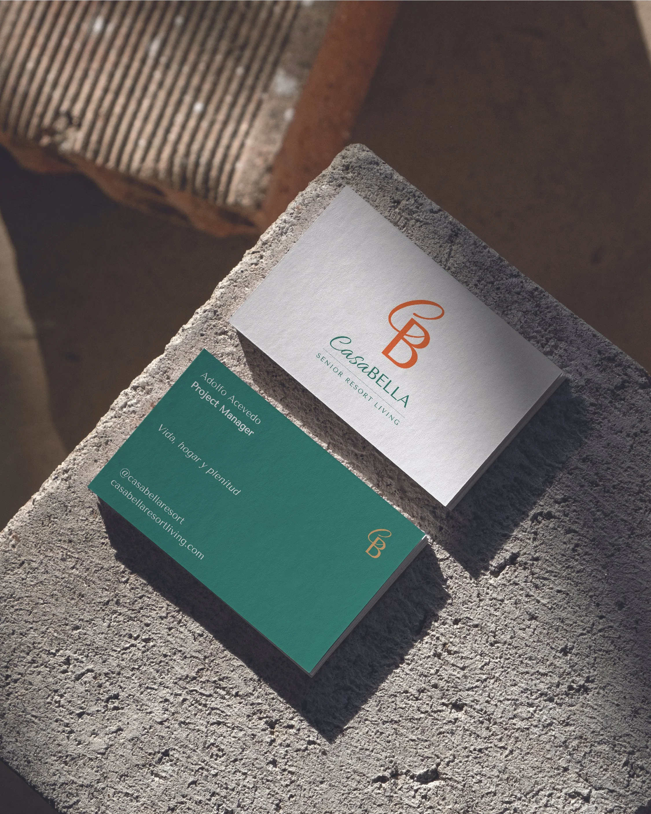 Business cards for Casabella Senior Resort Living placed on a rough concrete surface. One card displays the logo and name, the other shows contact details for Adolfo Acevedo, Project Manager.