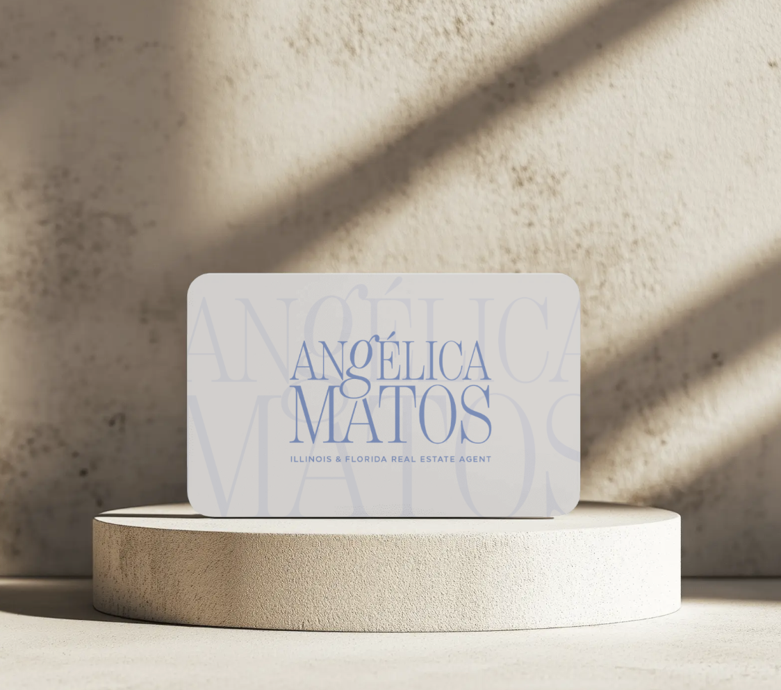 Business card for Angélica Matos, Illinois & Florida real estate agent, placed on a beige circular platform with shadows on a beige textured wall background.