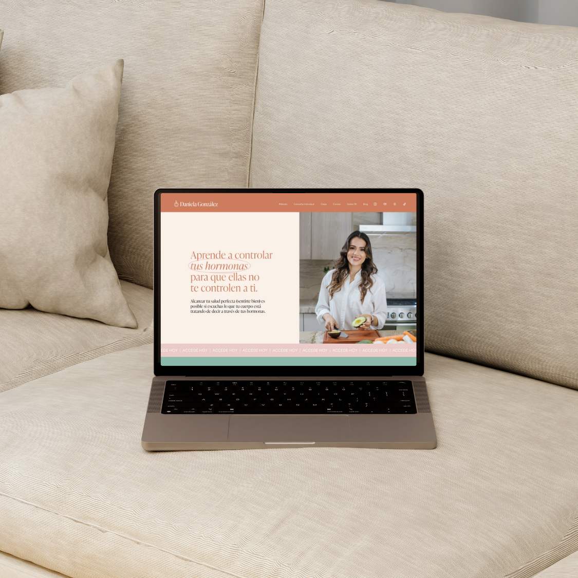 A laptop on a beige couch displaying a website about hormone control, featuring a woman in a white shirt preparing food in a modern kitchen.