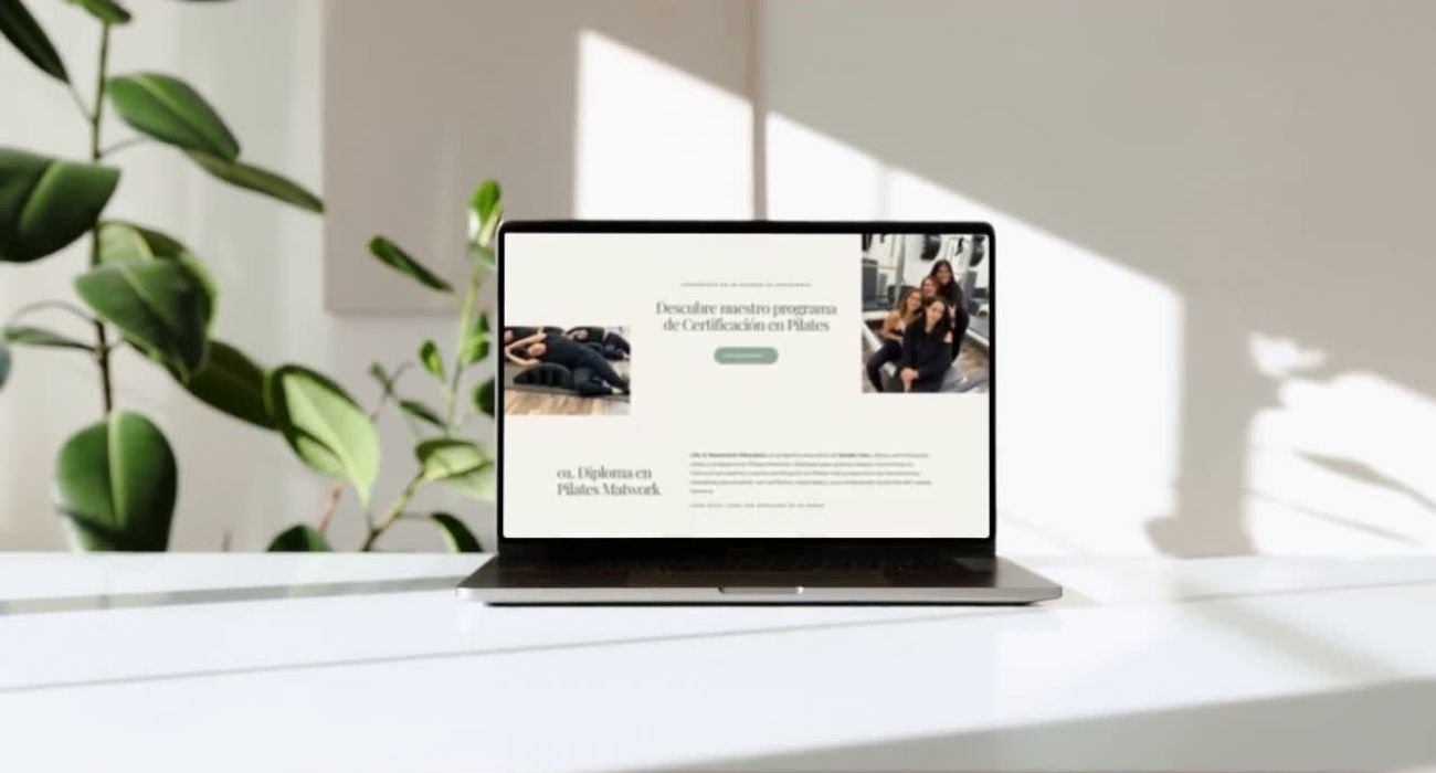 Laptop on a white table displaying a website about Pilates certification course with images of people doing Pilates, in a bright room with a green plant and sunlight.