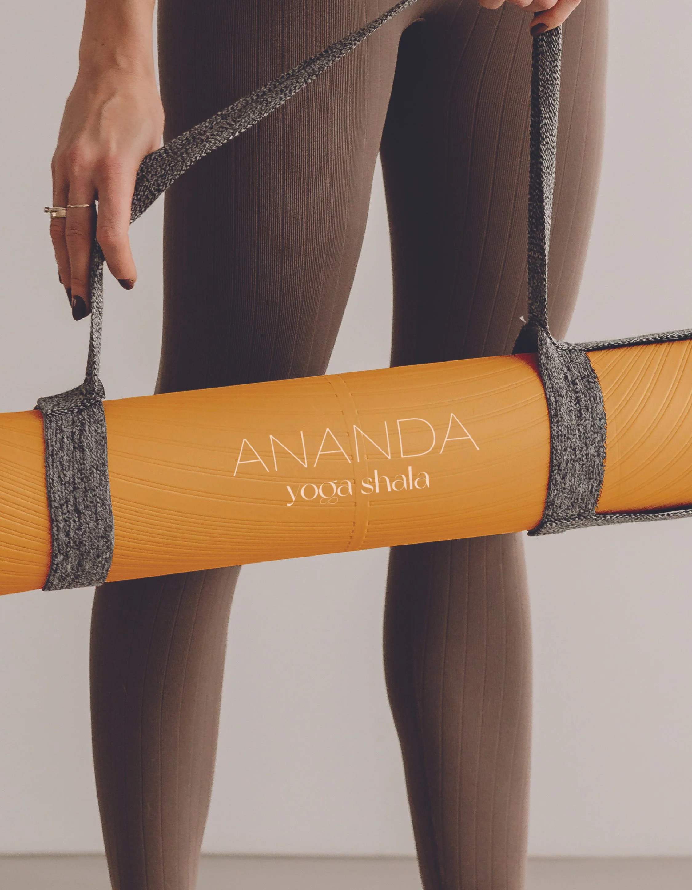 Person holding an orange yoga mat with the words 'ANANDA yoga shala' printed on it.