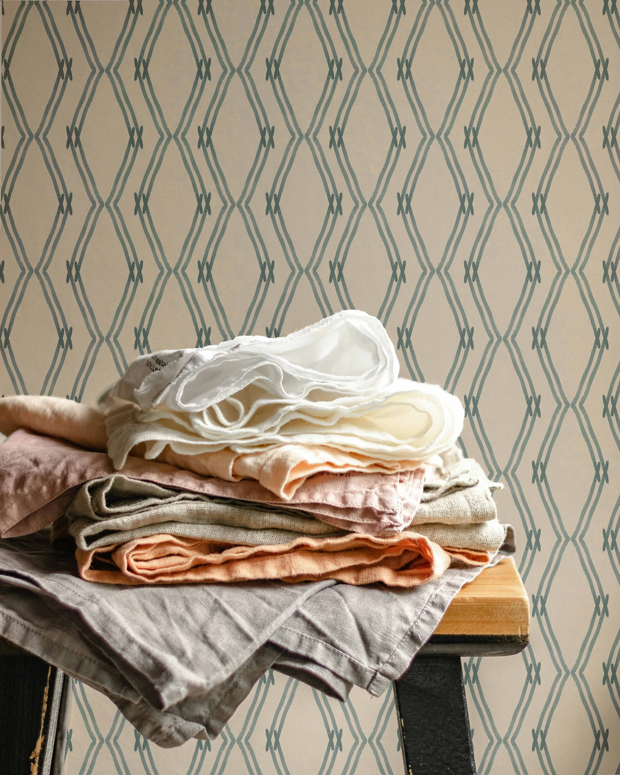 A stack of folded clothes on a wooden surface against a patterned wall.