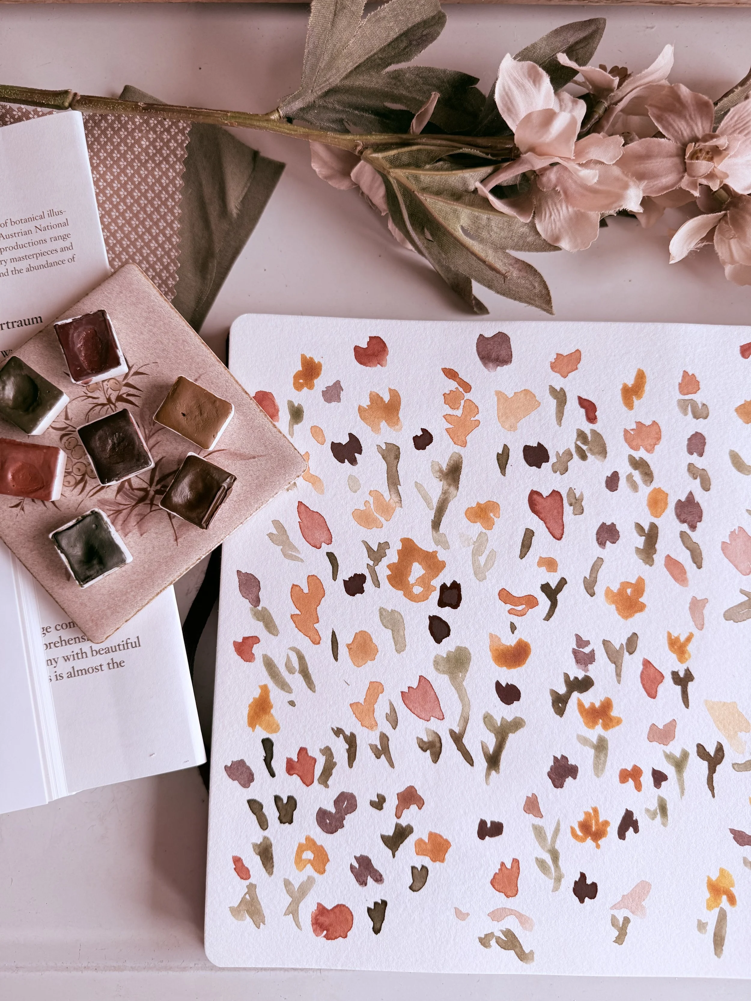 Flatlay of earth tone watercolors and a loose watercolor wildflower painting with flowers