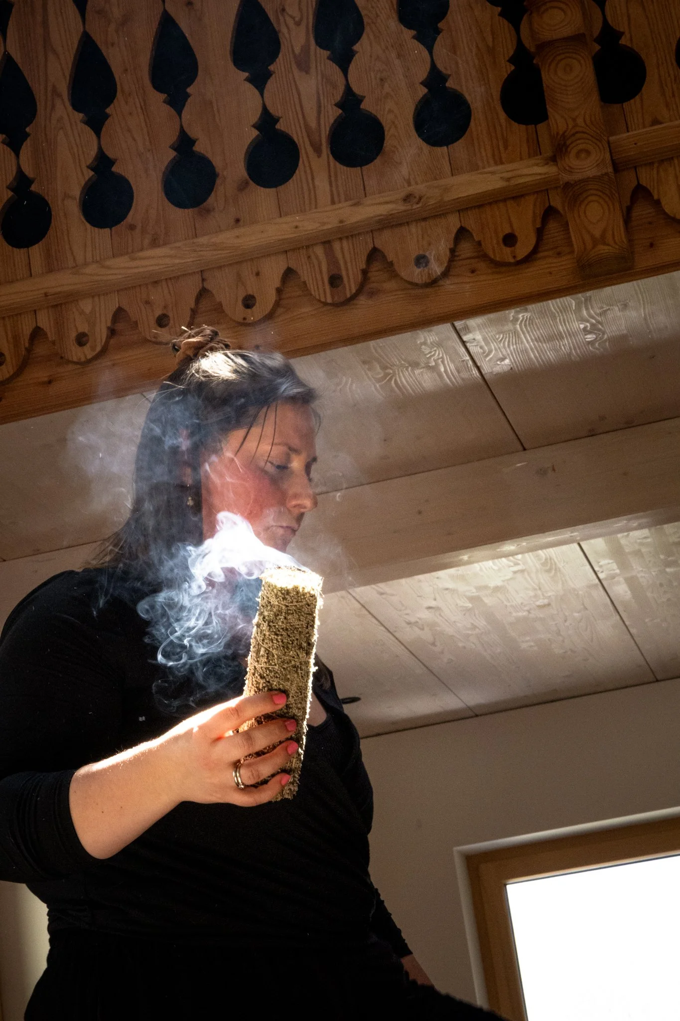 retreat photography - A woman with long dark hair tied back, wearing a black long-sleeved shirt, holding a cylindrical object with smoke rising from it.