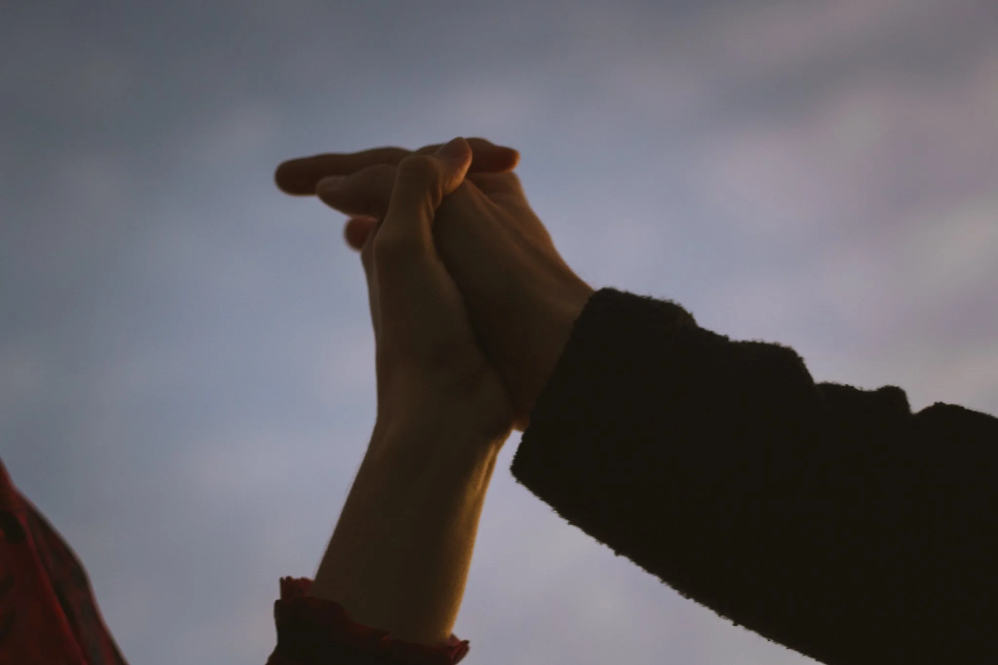 couples photoshoot - Two hands, one adult and one child, clasped together against a dusky sky.
