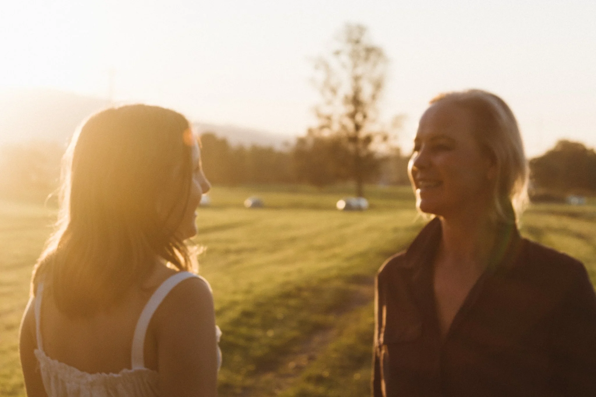 family photoshoot - a mother and her daughter are conversing outdoors during sunset, with a tree and cars in the background.