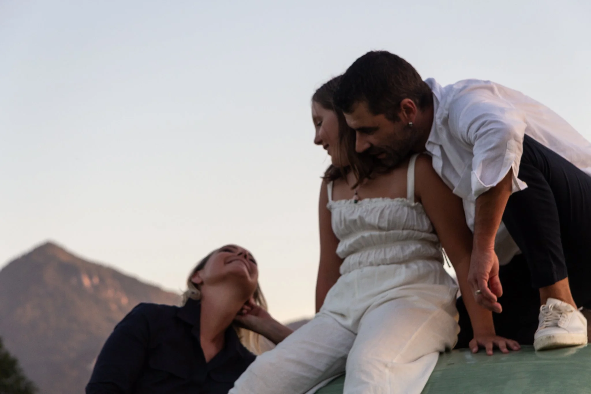 family photoshoot - Three people are engaging in a playful activity outdoors at sunset, a women, a daughter and one man, with mountains in the background.