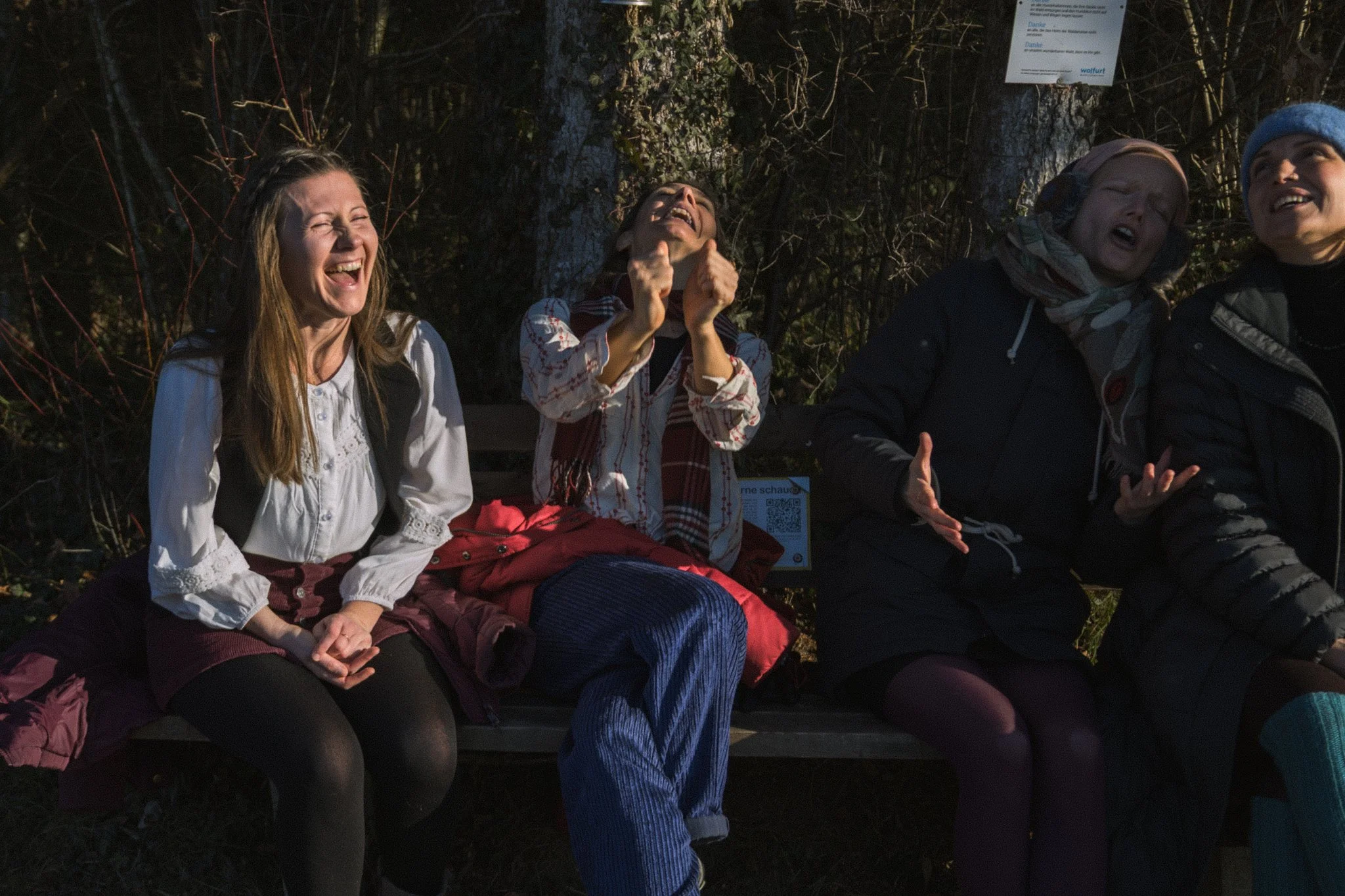 friends photoshoot - Four women sitting outdoors in a wooded area, laughing and enjoying themselves.