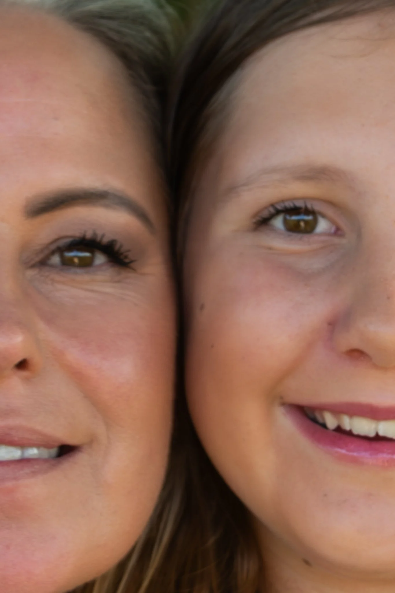family photoshoot - Close-up of two smiling women with their faces pressed closely together, showing their eyes, eyebrows, and part of their cheeks.