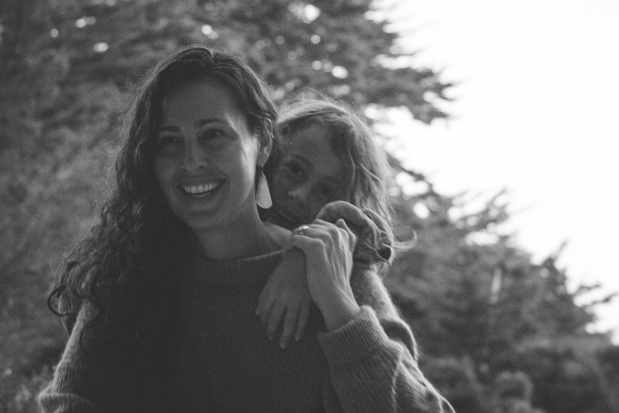 family photo shoot - a mother and her son smiling and embracing outdoors, with trees in the background, in black and white.