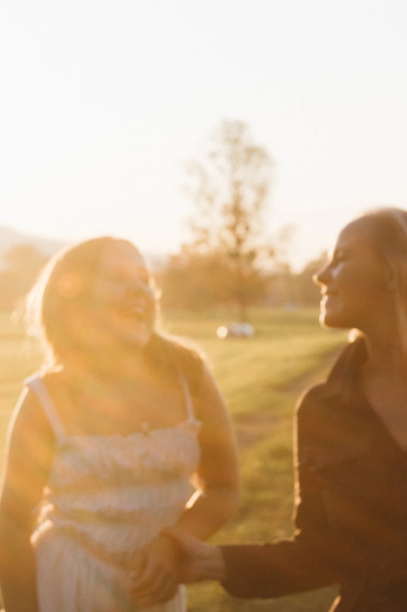 family photoshoot - A mother and her daughteroutdoors in warm sunlight, with trees in the background. laughing at each other