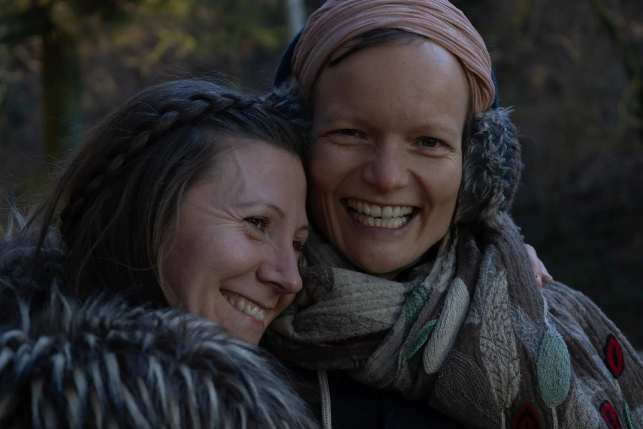 friends photoshoot - Two women smiling and hugging outdoors in a forest setting.