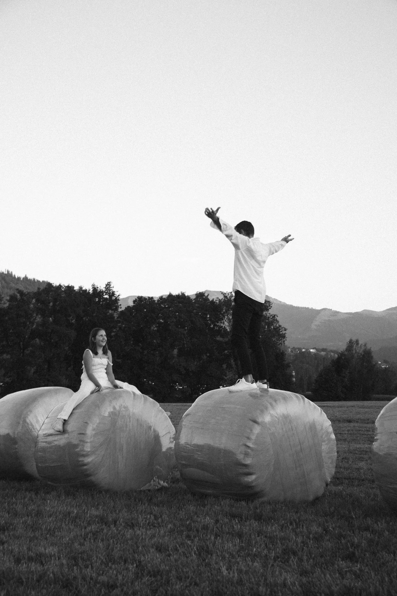 family photoshoot - People atop large hay bales in an open field during sunset, with a mountain range in the background.