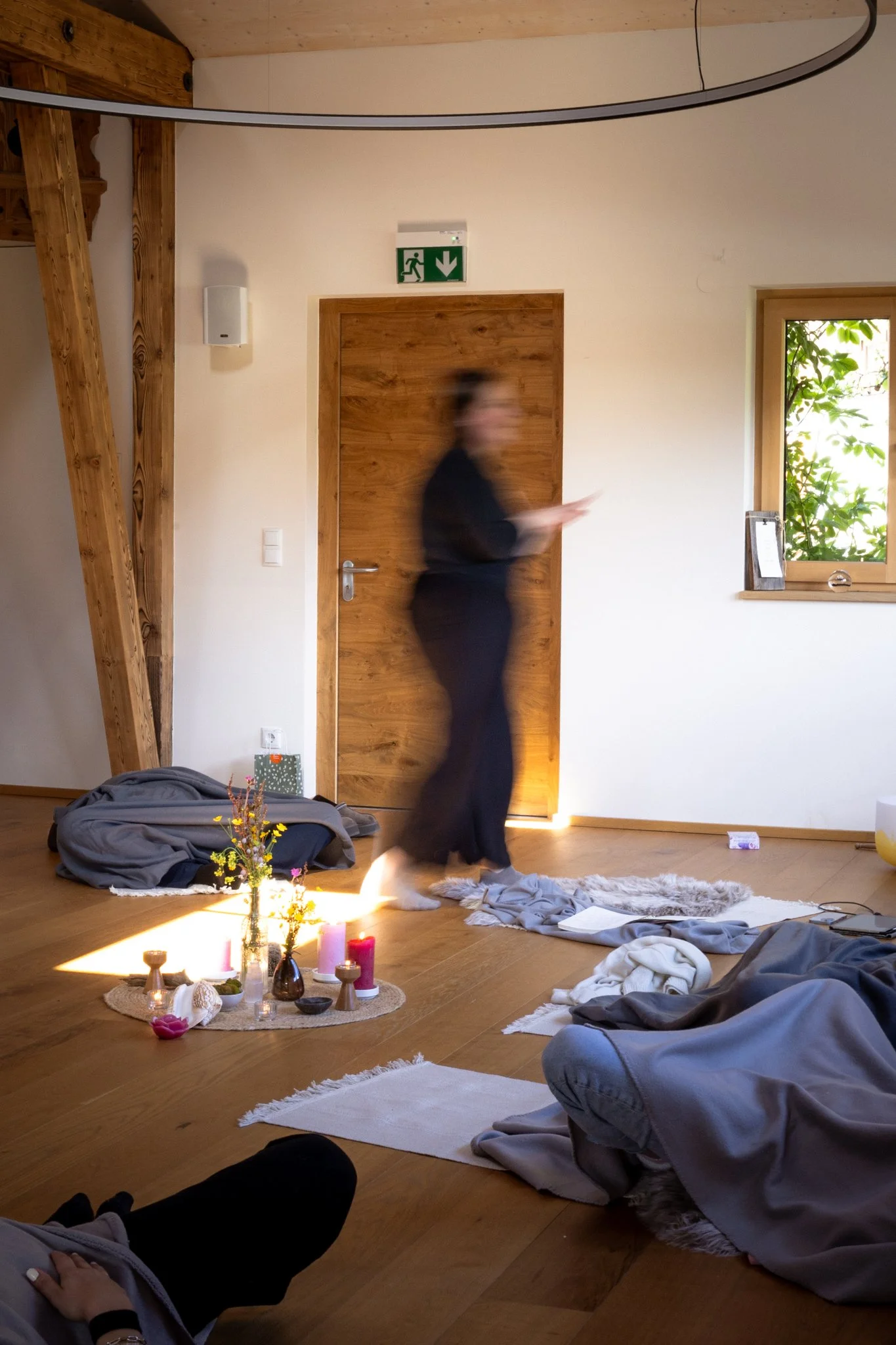 retreat photography - A blurry woman walking in a cozy room with wooden floors, decorated with candles, flowers, and a small altar on the floor.