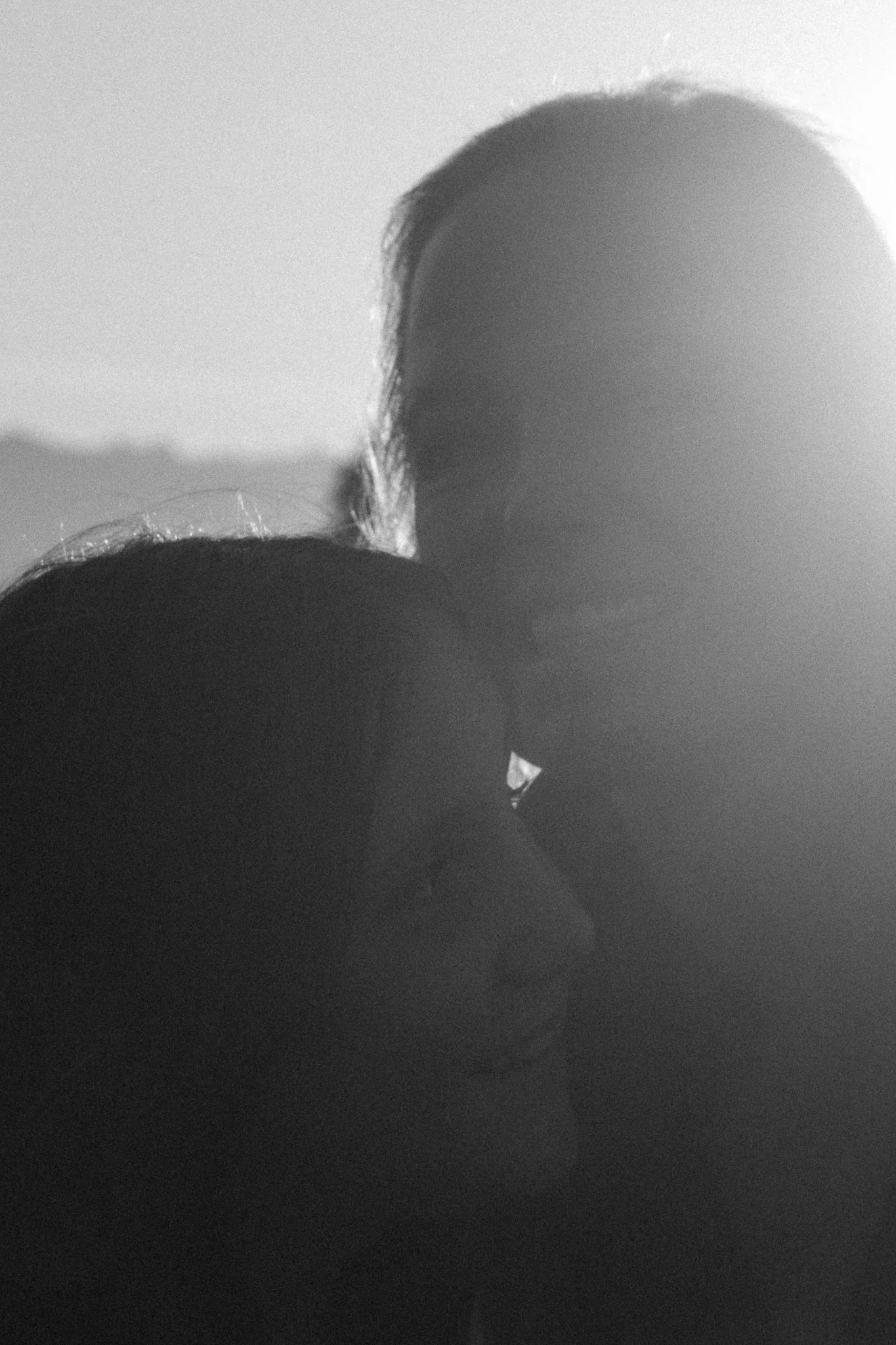 family photoshoot - Black and white photograph of a person's head with long hair, looking to the side, backlit with a bright light source behind them.