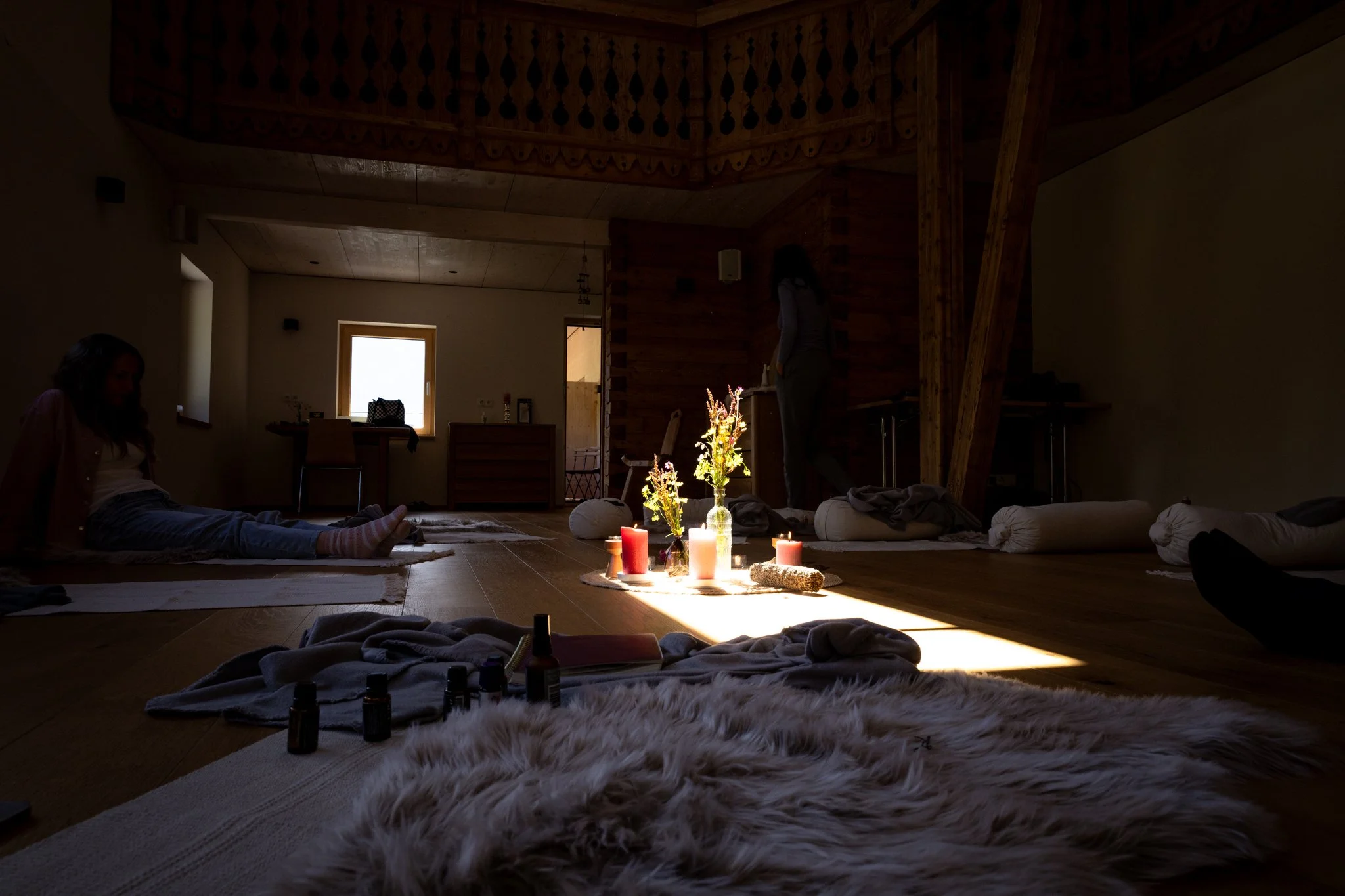 retreat photography - People lying on their backs on mats in a dimly lit room decorated with candles and flowers, practicing  meditation.