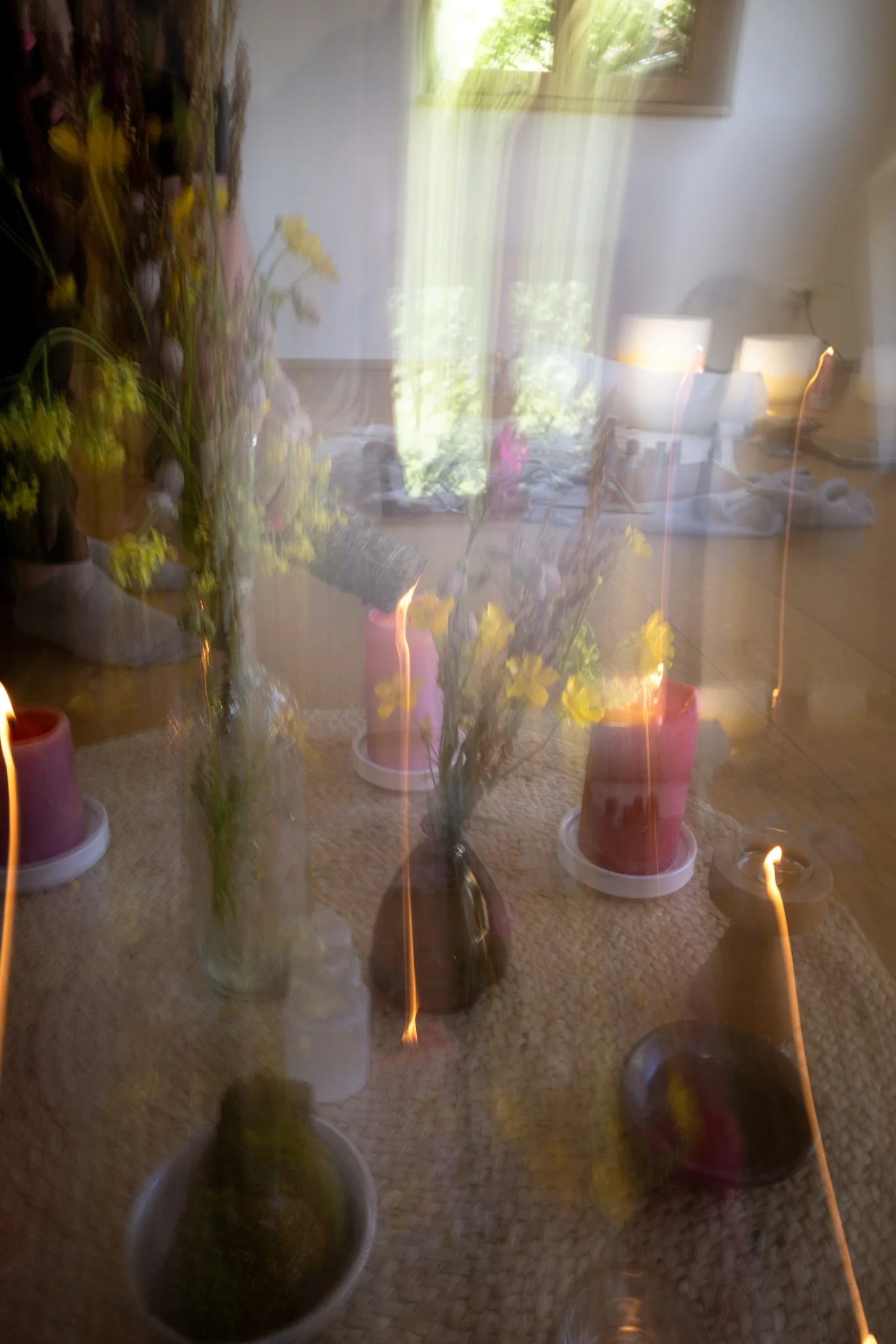 retreat photography - Blurred image of flowers in vases on a table with candles, reflections, and a window in the background.