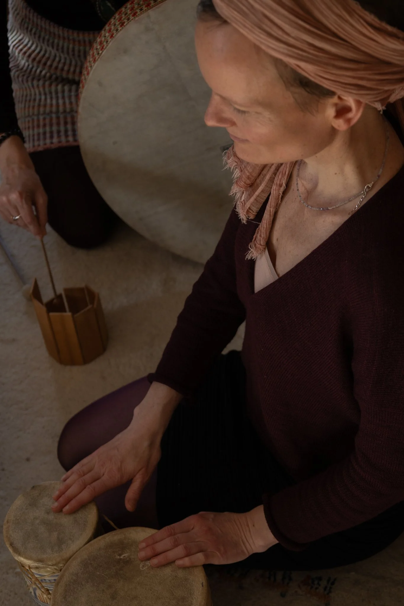 friends photoshoot - A woman with reddish hair and freckles sitting at a table, pressing her hands on stones or large objects, in an indoor setting.