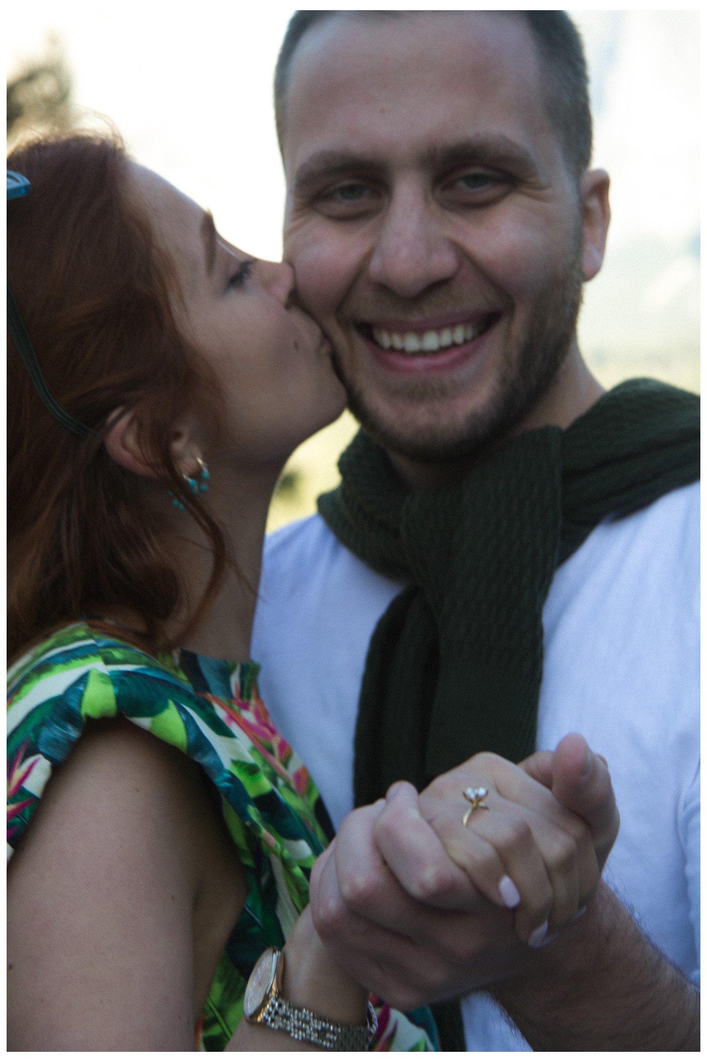 engagement / couple - newly engaged couple, showing the ring. she's kissing his cheek and he islooking into the camera