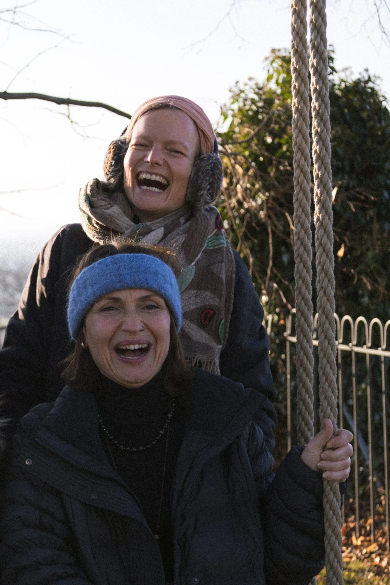 friends photoshoot - Two women smiling, one holding a rope, outdoors in a park on a sunny day.