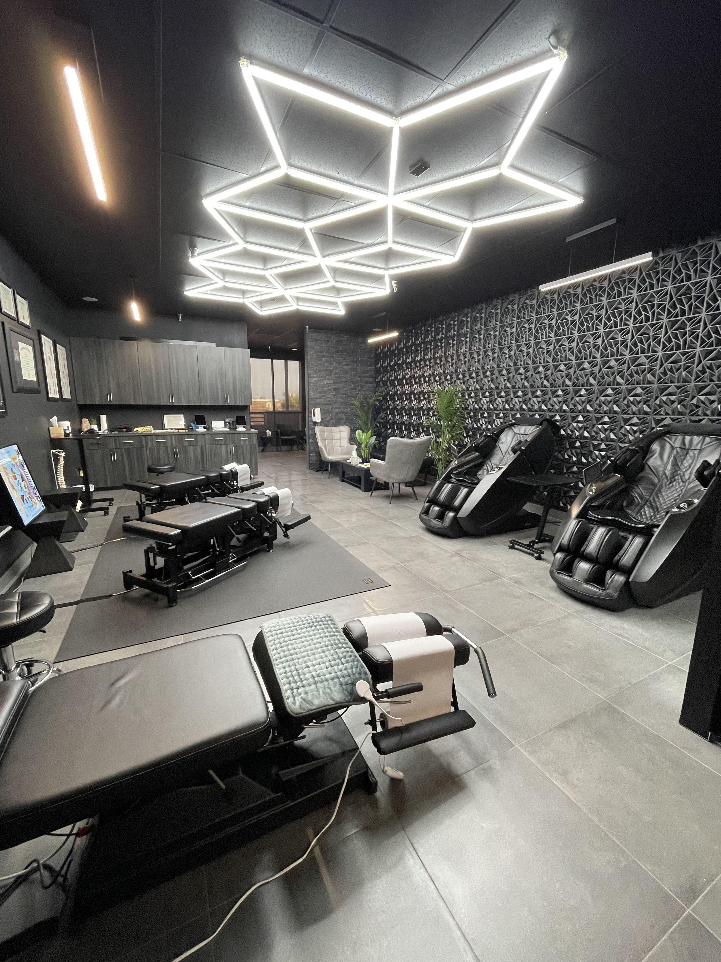 Interior of Elite Body Mind Chiropractic with modern geometric light fixture, massage chairs, and chiropractic tables.