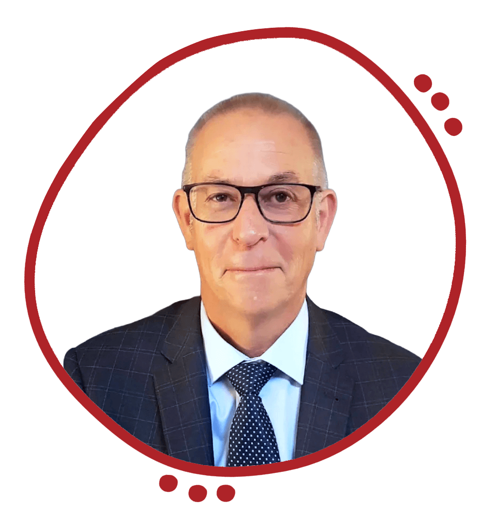 Portrait of a middle-aged man wearing glasses, a dark checkered suit, a white shirt, and a polka dot tie, standing against a plain dark wall.