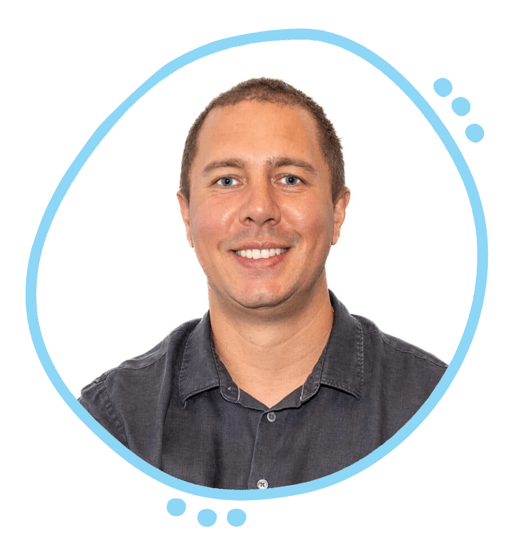 A smiling man with short light brown hair and blue eyes, wearing a dark gray shirt, posed against a white background.