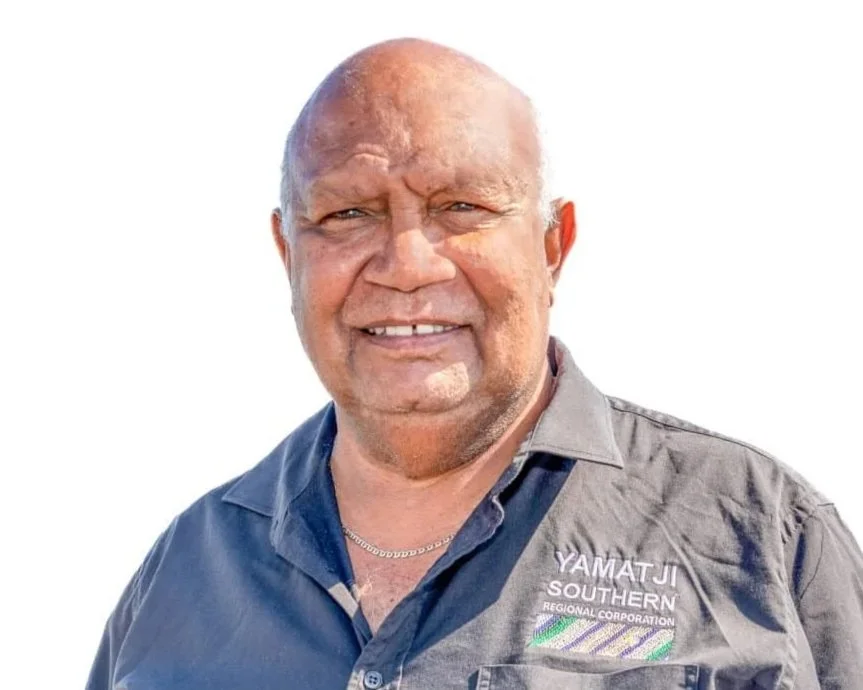 A smiling man wearing a dark gray shirt with patch that reads Yamatji Southern Regional Corporation, standing outdoors against a bright sky.