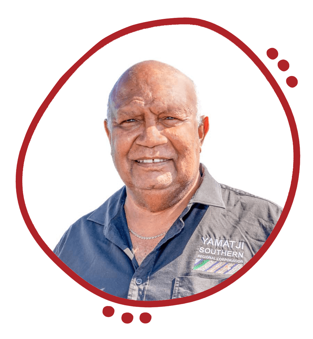 A smiling man wearing a dark gray shirt with patch that reads Yamatji Southern Regional Corporation, standing outdoors against a bright sky.
