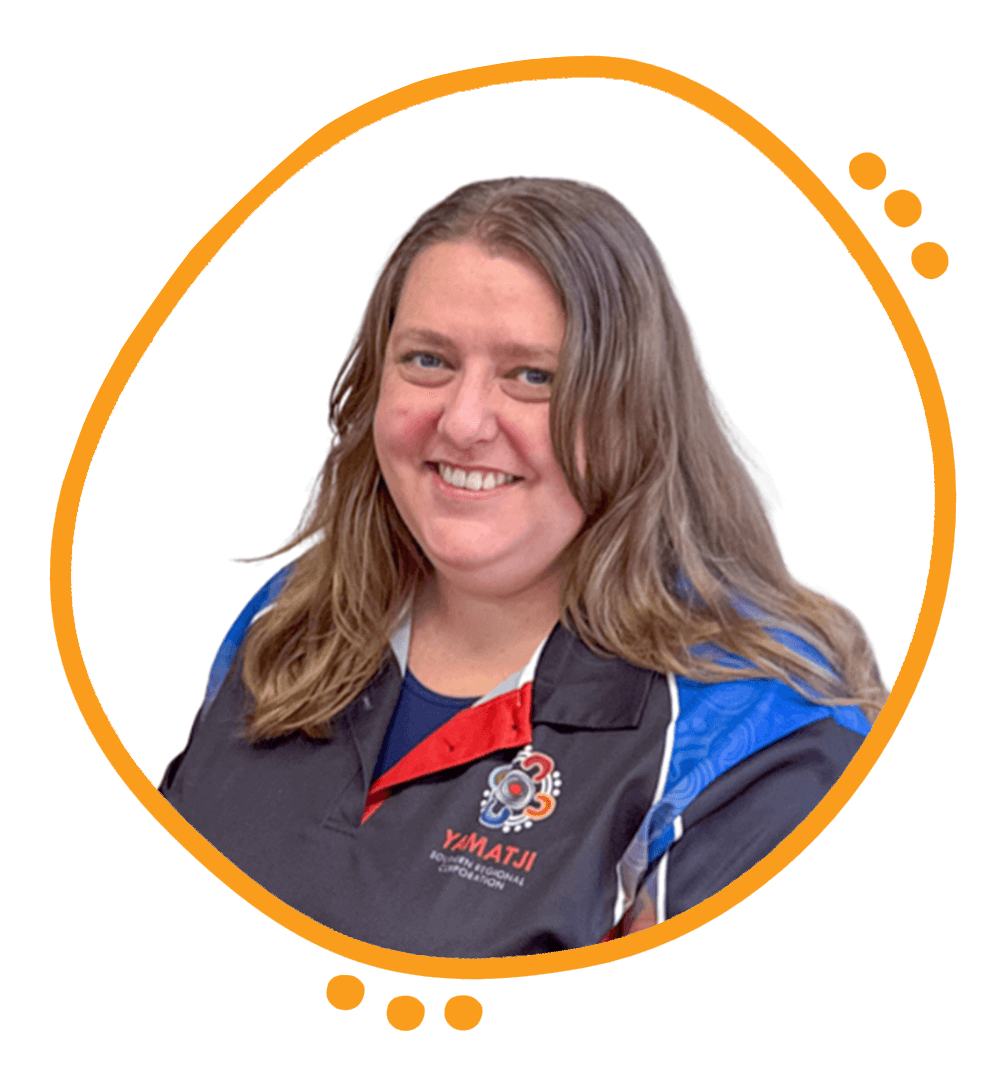 A woman with shoulder-length brown hair, wearing earrings, a necklace, a white blazer, and a floral blouse, smiling at the camera against a white background.