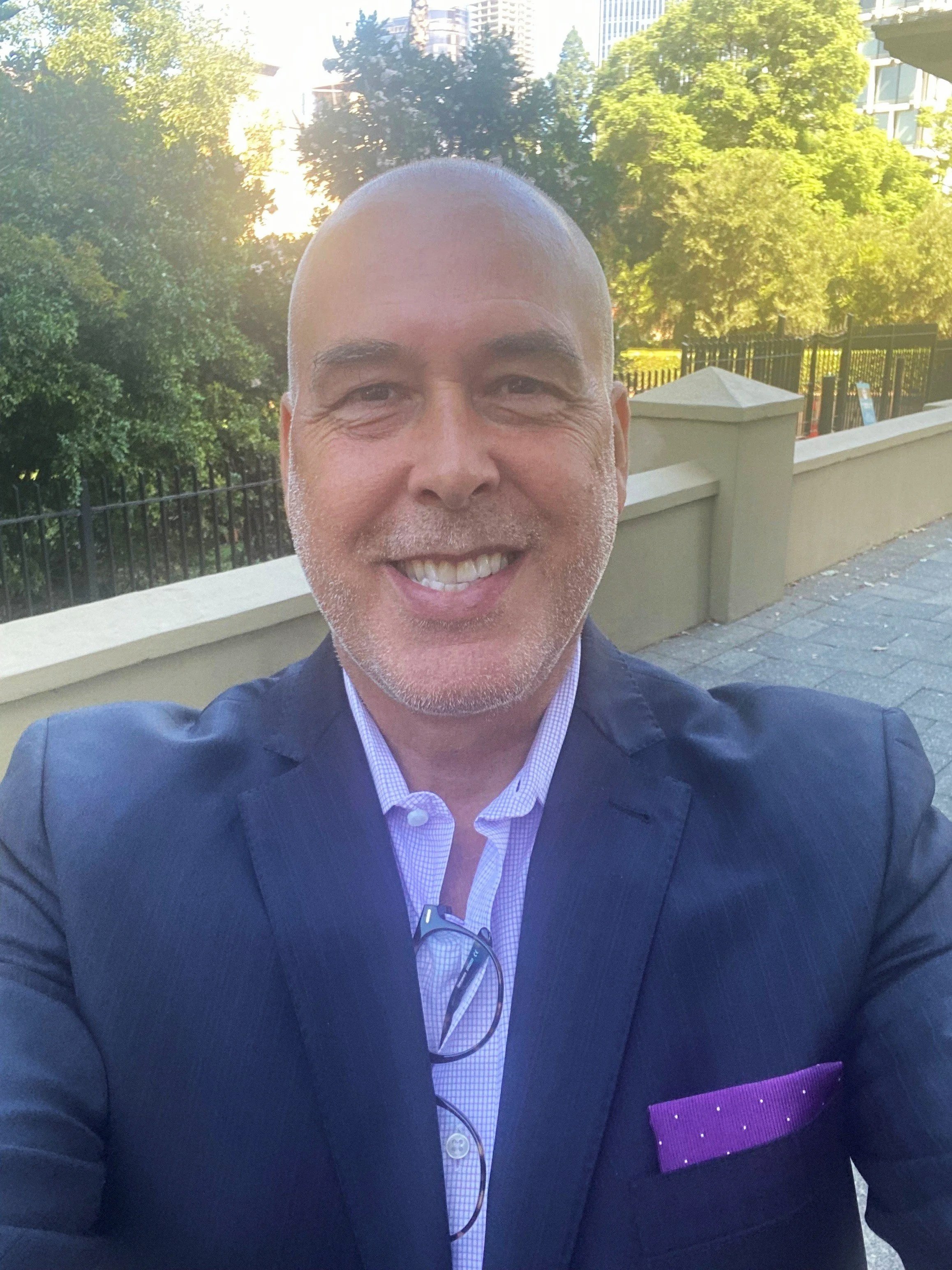 Smiling man with a shaved head wearing a dark pinstripe suit and light blue shirt.