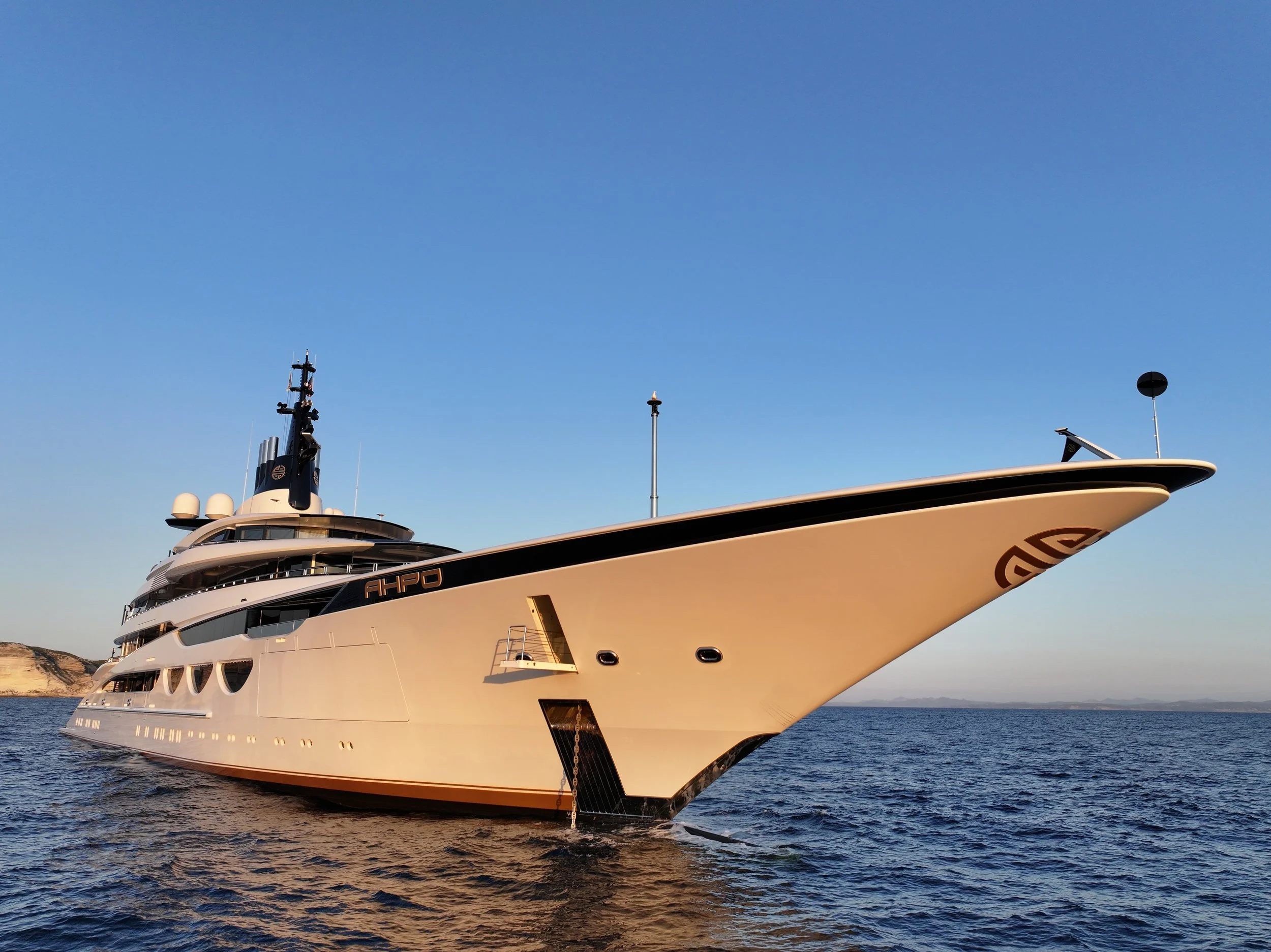 A luxury yacht sailing on the water during sunset, with a scenic shoreline in the background.