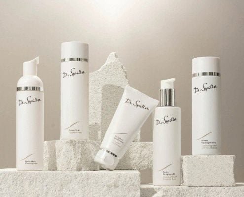 Collection of white skincare bottles and tubes on white brick and plaster backdrop