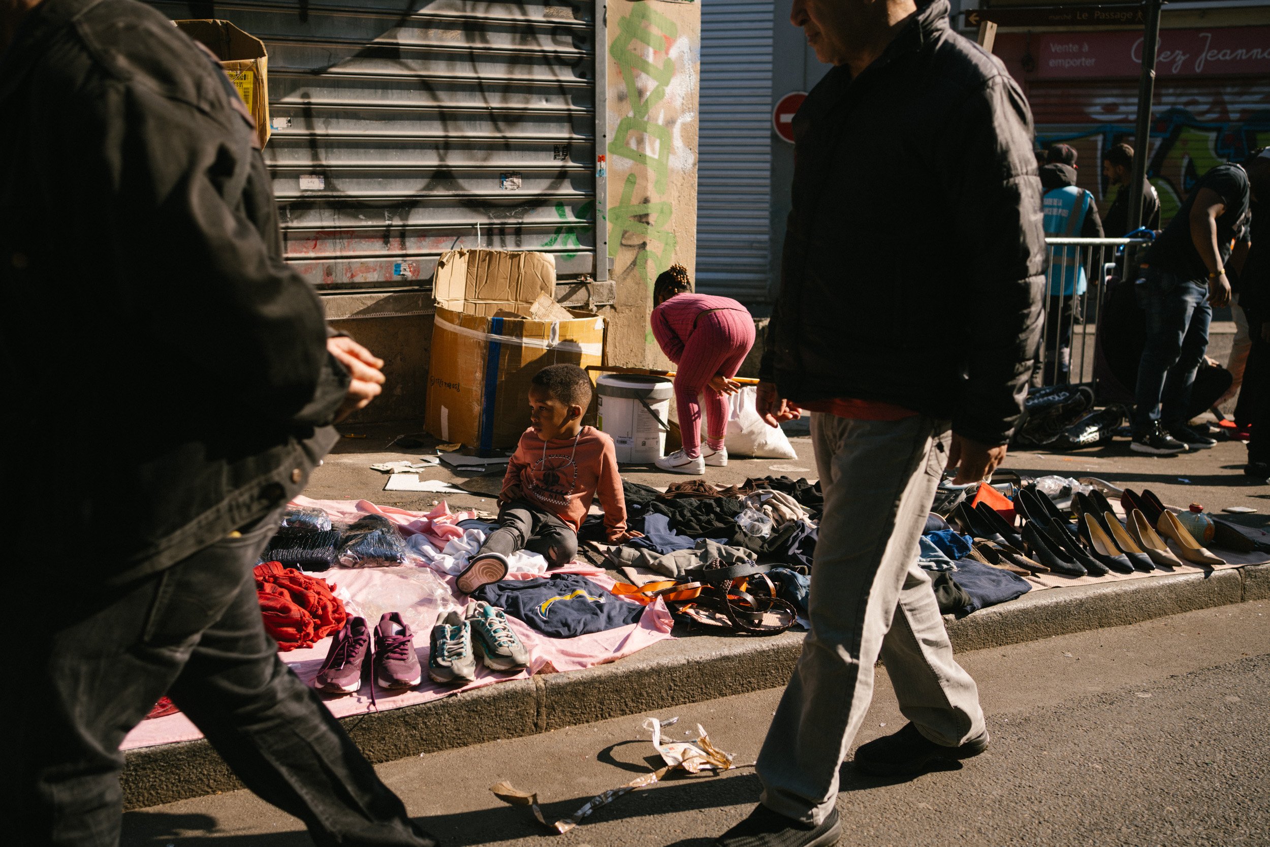 Menschen verkaufen Kleidung und Schuhe auf einem Straßen-Flohmarkt, im Hintergrund sind Graffiti an einer Wand.