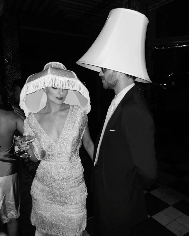Well-dressed man and woman wearing lampshades as hats
