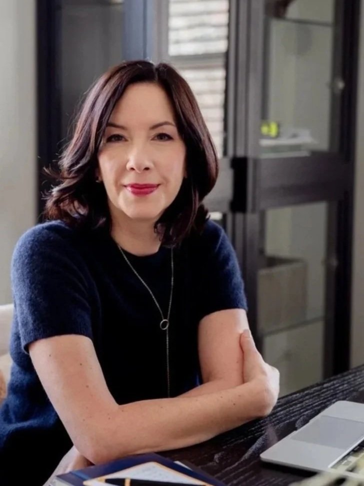 executive coach for biotech and pharma leaders, Angela Justice, at desk smiling with arms crossed