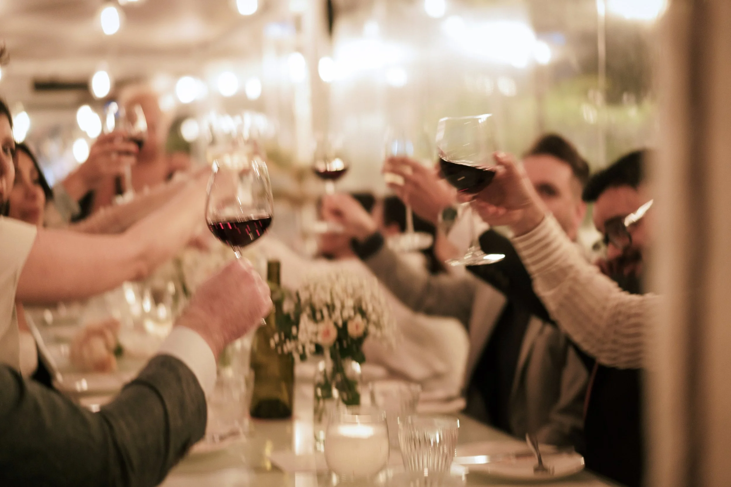 People raising glasses of red wine in a toast at a celebratory dinner party.