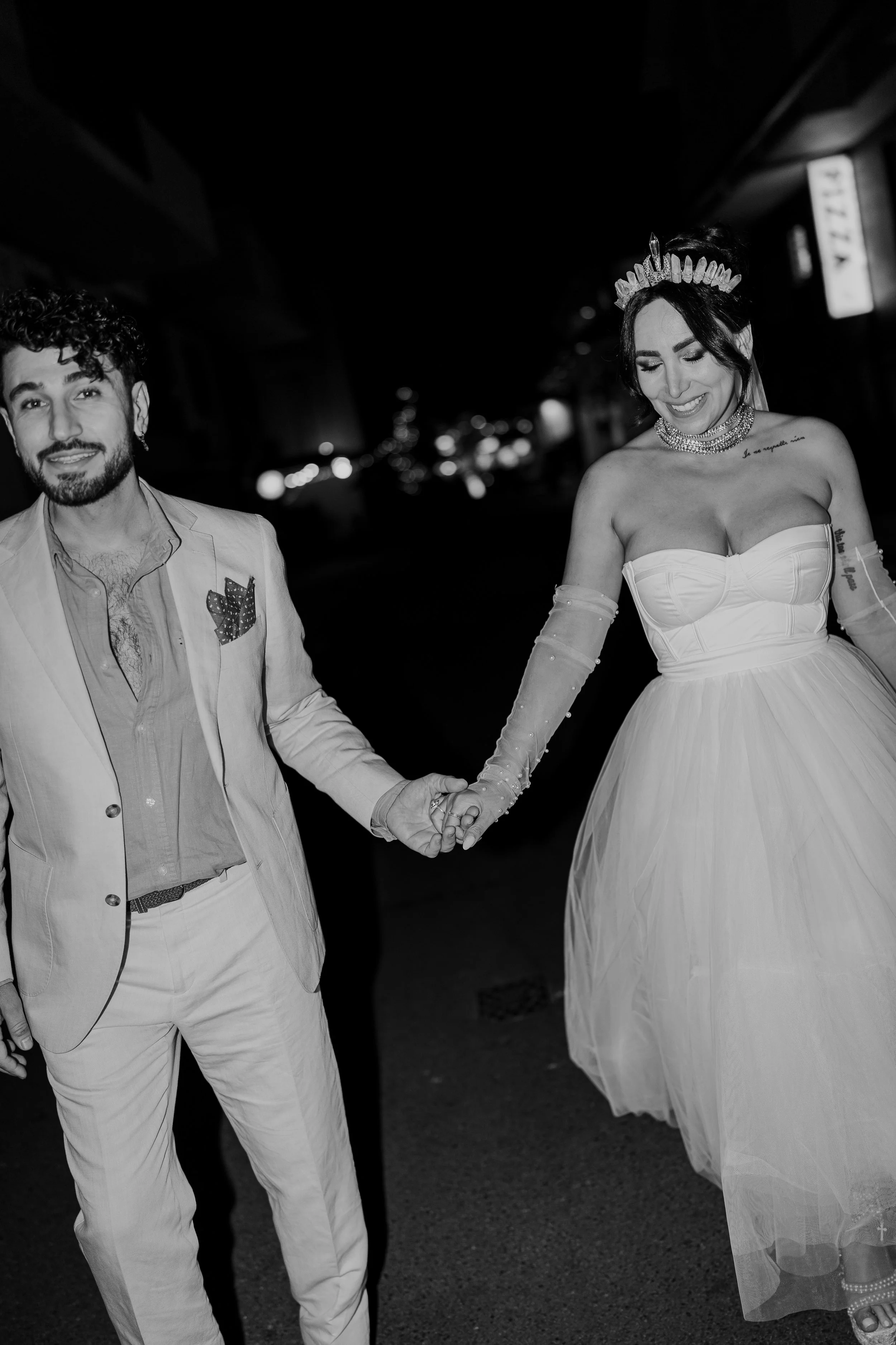 A couple holding hands at night, the woman in a wedding dress and the man in a suit.