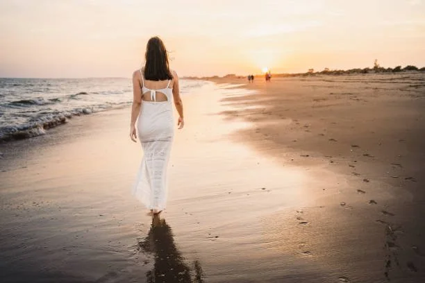 Woman walking along the beach at sunset, representing transit charts and personal evolution.